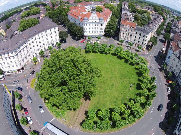 Der Borsig-Platz. In der MItte eine Wiese. Um den Platz herum führt eine Straße. Am Rande stehen Häuser